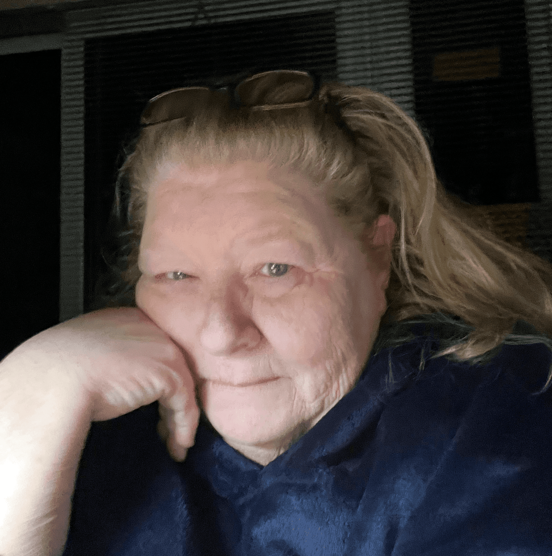 Close up photo of a pale faced women with blue eyes, wearing a fuzzy dark blue jacket. She has her right hand tucked under her chin and she is looking at the camera.