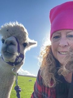 Close up of  woman in a pink wool hat standing next to a llama