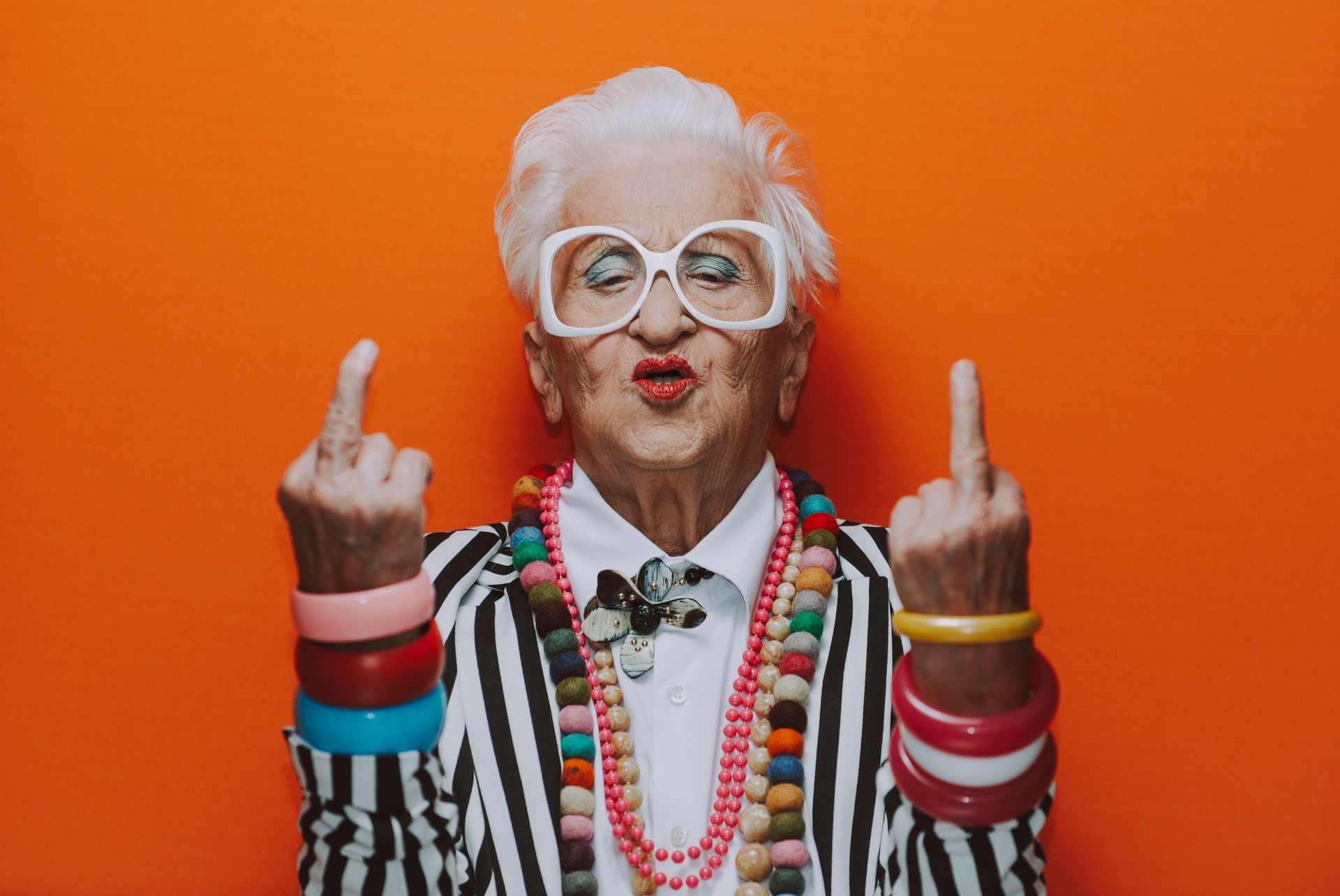 Portrait Of Senior Woman Wearing Showing Obscene Gesture Against Red Background