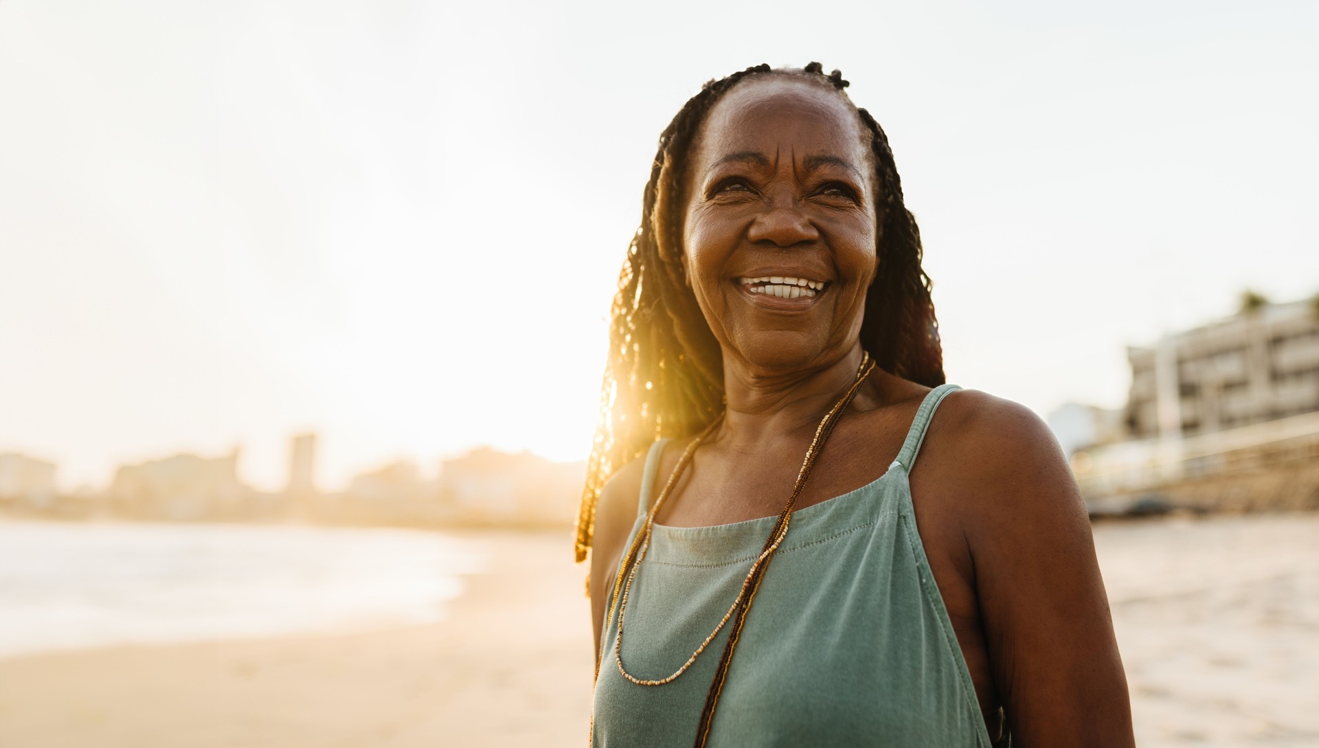 Joyful senior woman with braids smiles at the beach during sunset